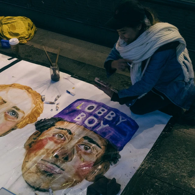 two face drawings with paint and pencil on a table