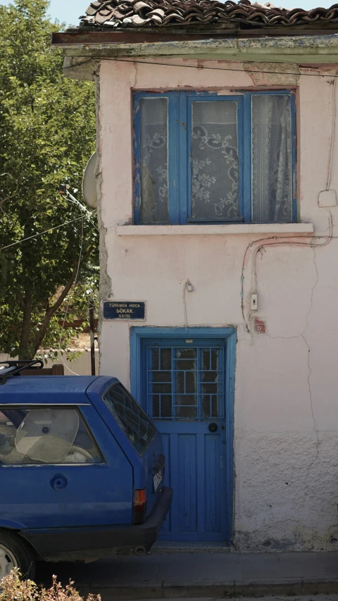 a pink building with blue shutters and a parked car