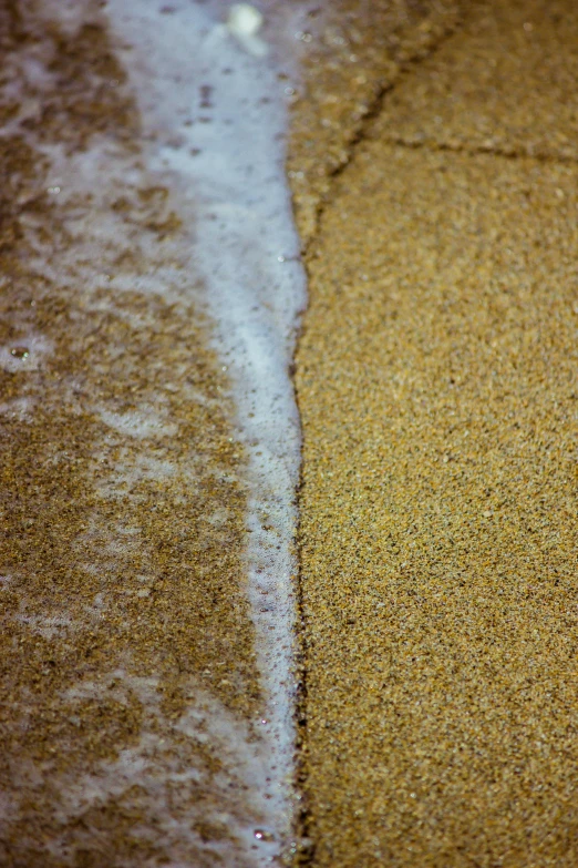 closeup of sand next to ocean and white surf