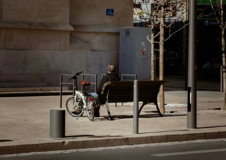 man in black jacket sitting on a bench with his bike next to him