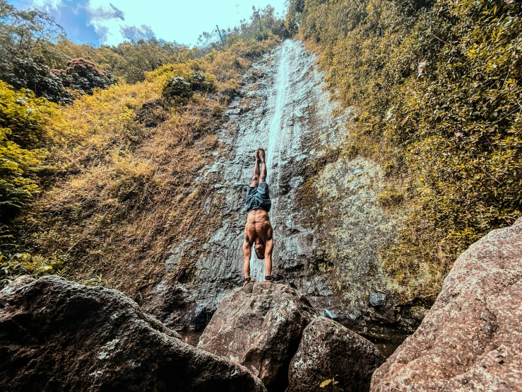 man is climbing over rocks and reaching for his top