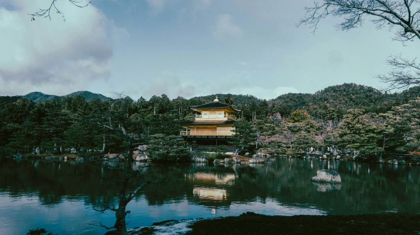 a small building with the water in front is surrounded by trees