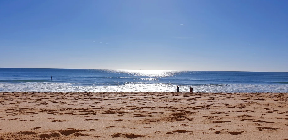 two people sitting on a beach while the sun reflects in the water