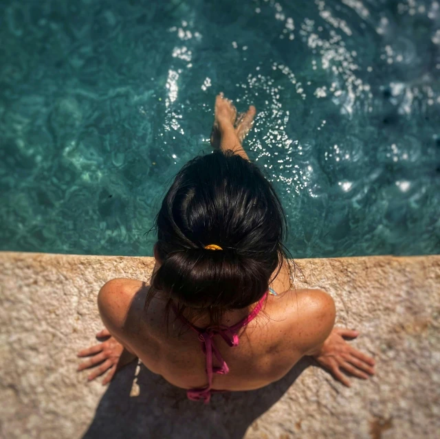 a woman is sitting on the edge of an ocean pool