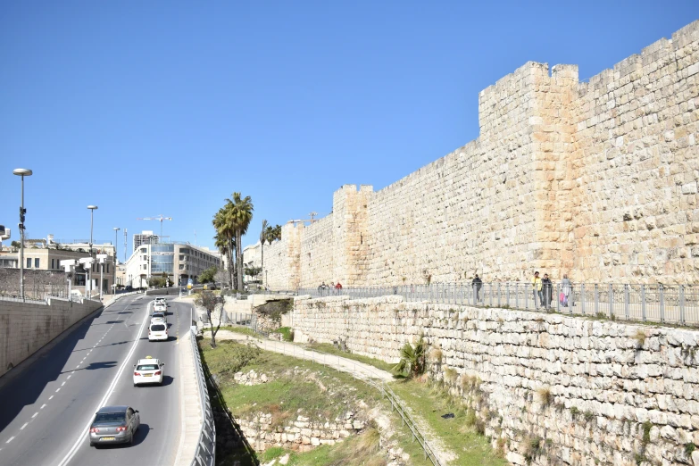 cars drive on a road near an old city wall