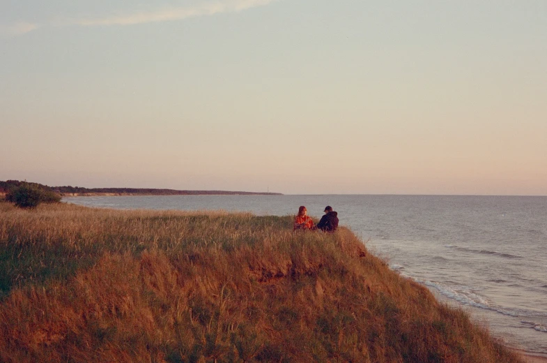 two people sitting on the shore of an empty beach