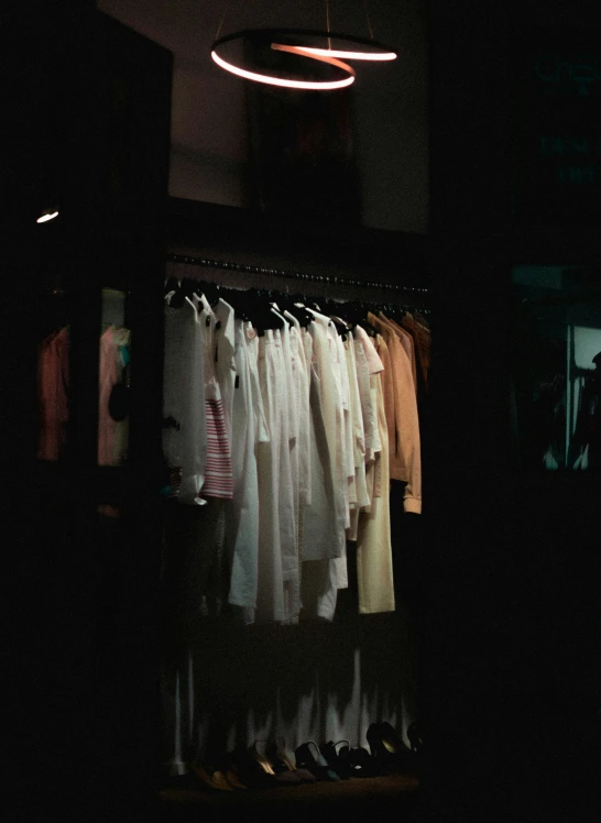 an illuminated closet with shoes and shirts hanging