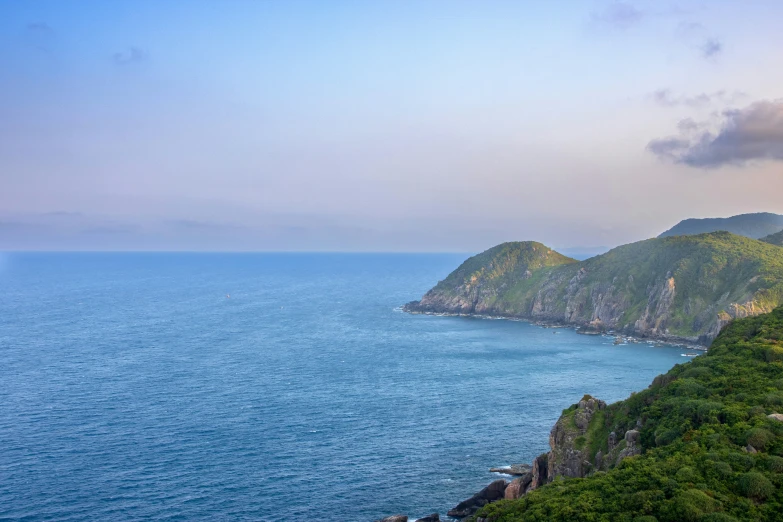 some green mountains are near the water and clouds