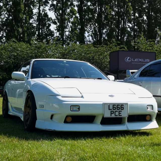 a white sports car is in the grass near some other cars