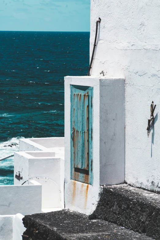 the small, worn out door is open on a white stucco building by the sea