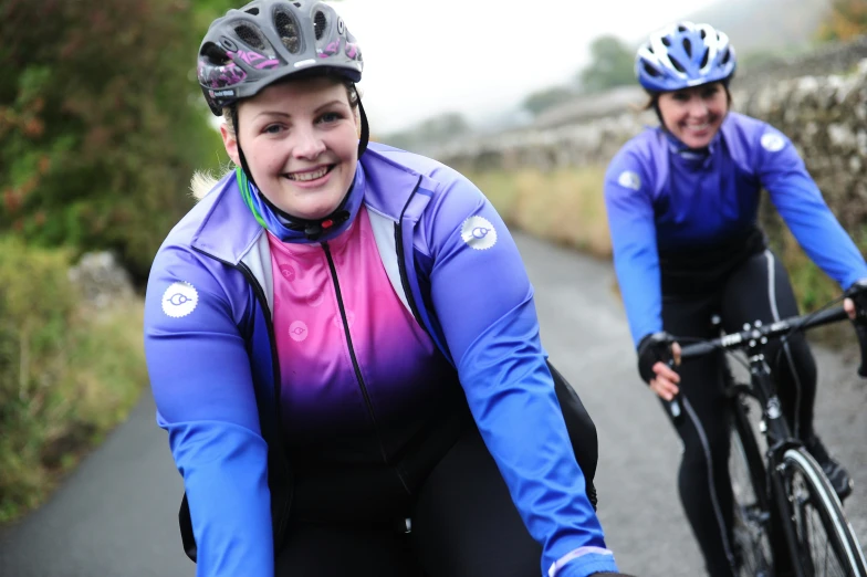 two women riding bicycles down the middle of a road