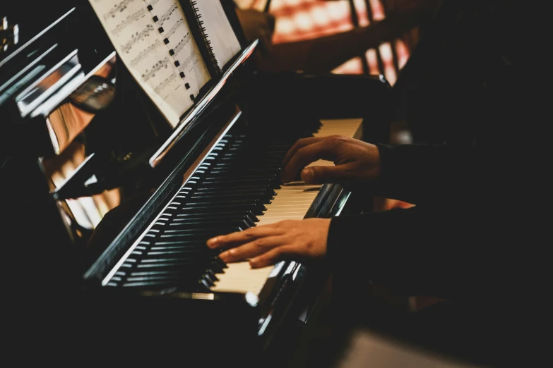 hands playing a piano with music sheets on display