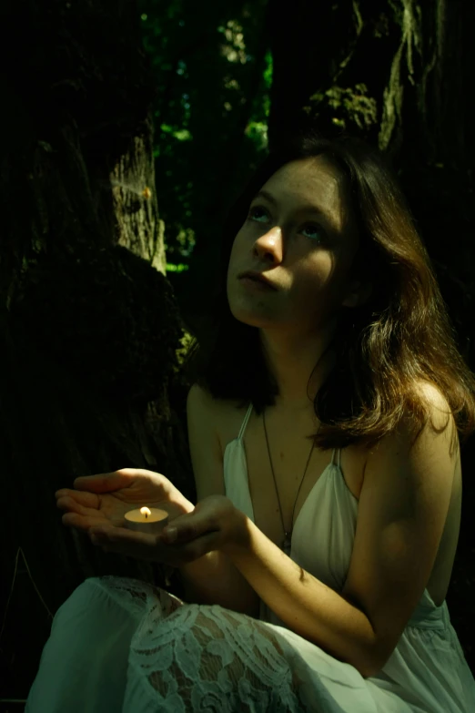 a girl sitting in a forest with her hands together and looking up