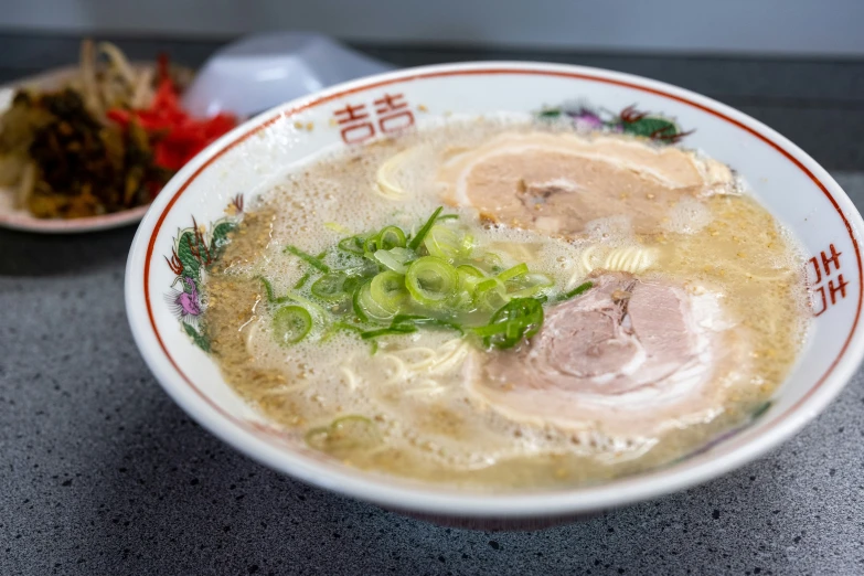 a bowl of chinese noodle soup with a plate of noodles and peppers