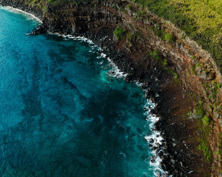 green hills and trees are above the ocean with a sandy beach