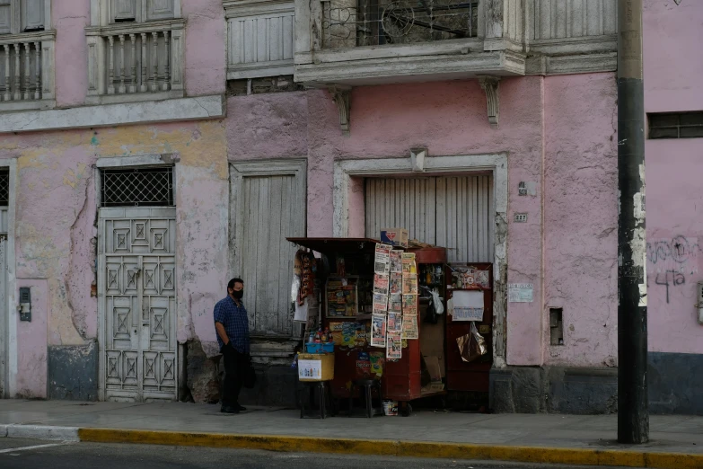 a person stands on a sidewalk next to a building with shutters