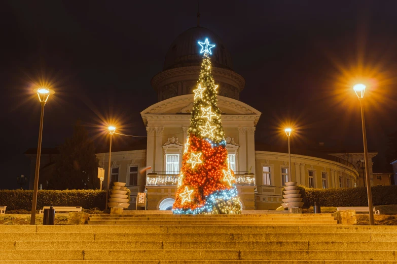 a lit up christmas tree at night in front of an old building