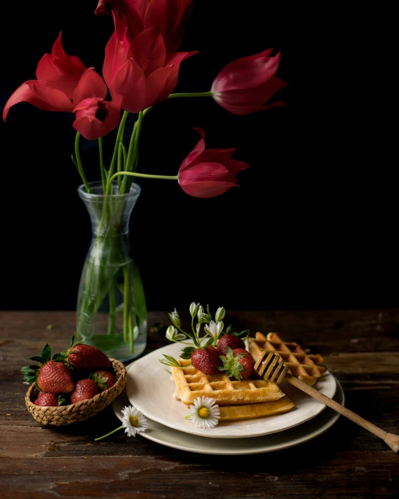 a plate with strawberries, waffles, and a bouquet of flowers