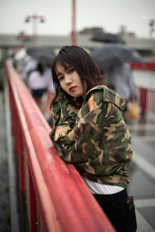a young lady in a camouflage jacket leaning against a rail