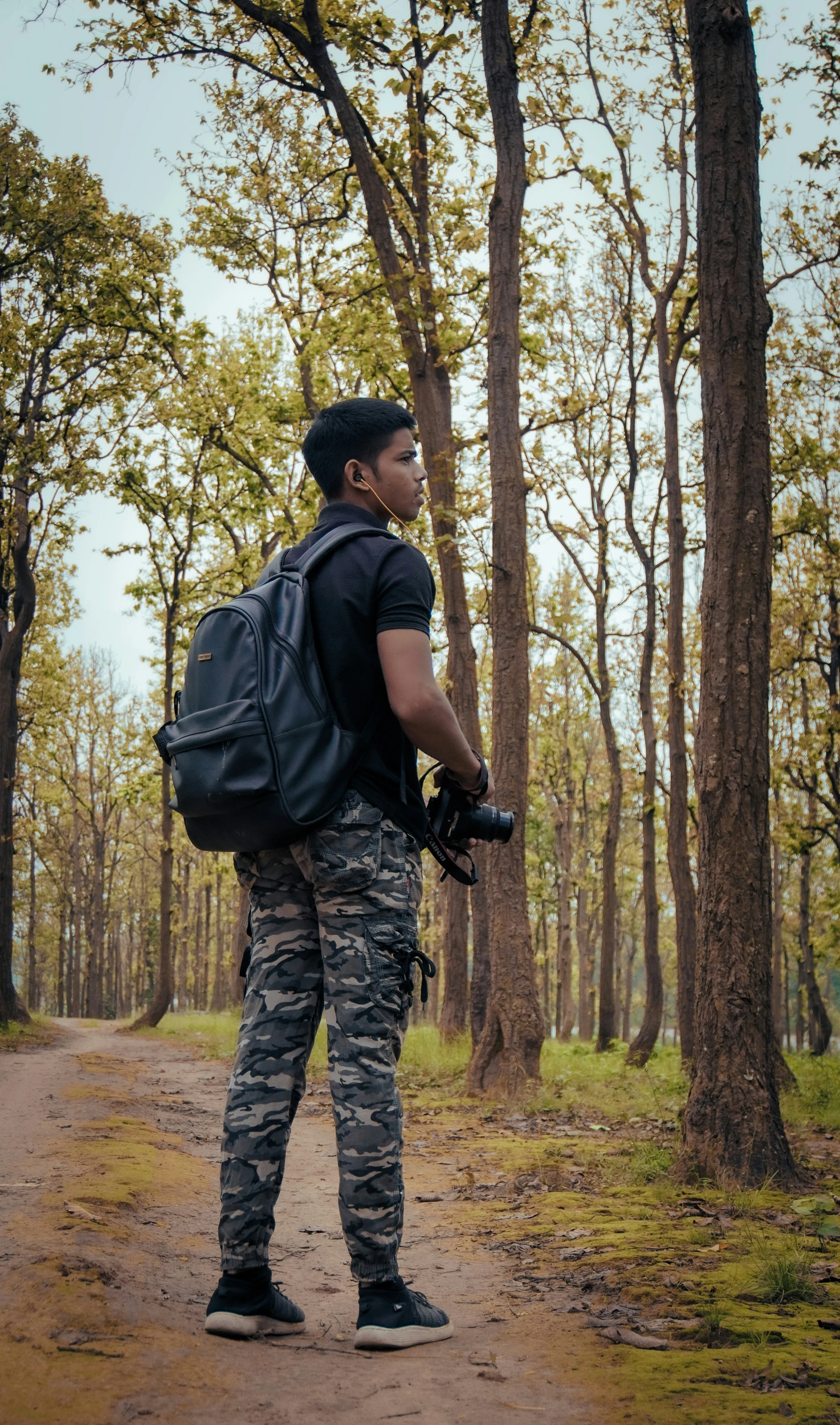 a man standing on a dirt road wearing a backpack and holding a camera