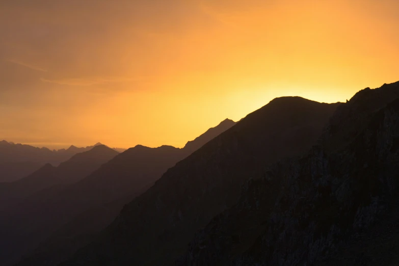 a silhouette of the mountains during sunset, with a yellow light shining