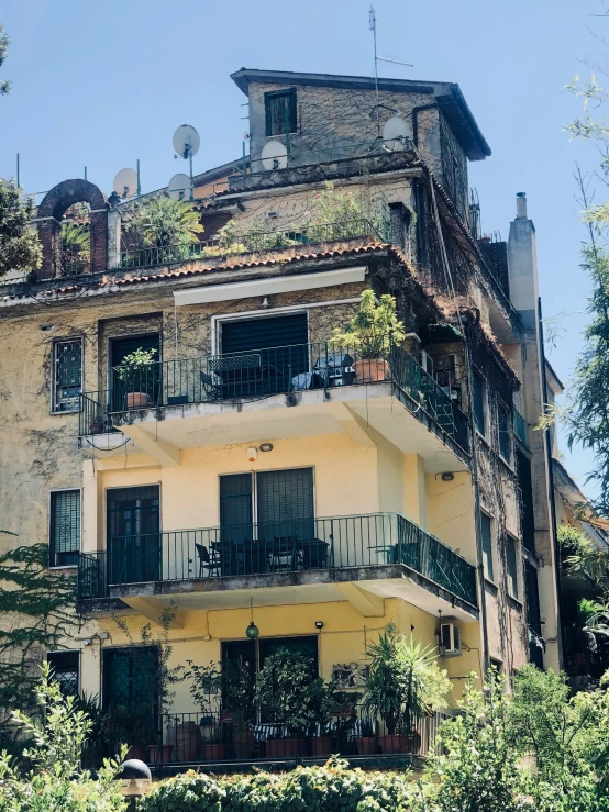 a yellow house with plants and balconies on the second story