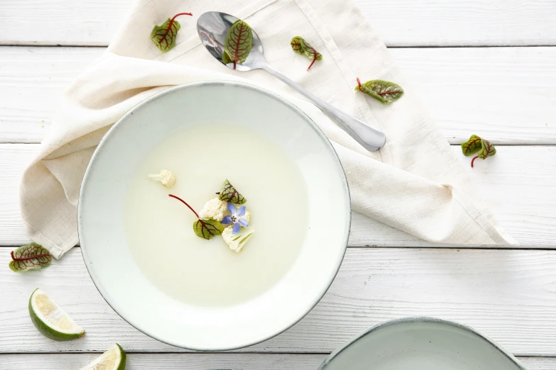 a white bowl of cream on a table with limes and leaves