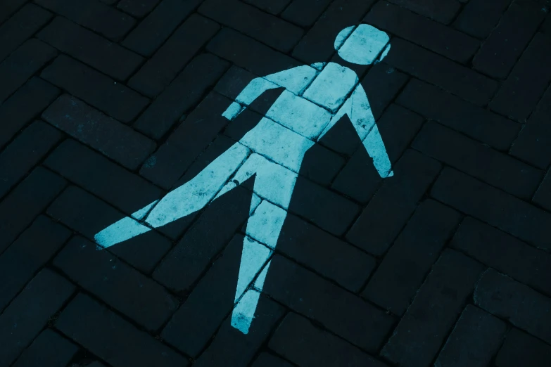 a person walks across a black pavement that is illuminated by a glowing blue pedestrian signal