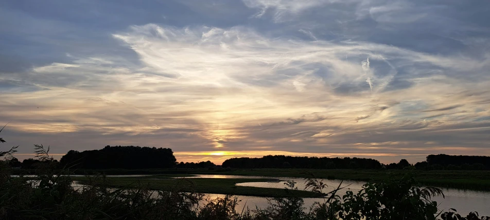 beautiful cloudy skies over an open field next to the water