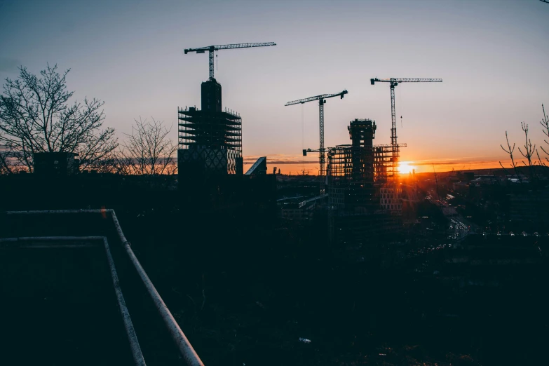 sun setting over some construction cranes in a city