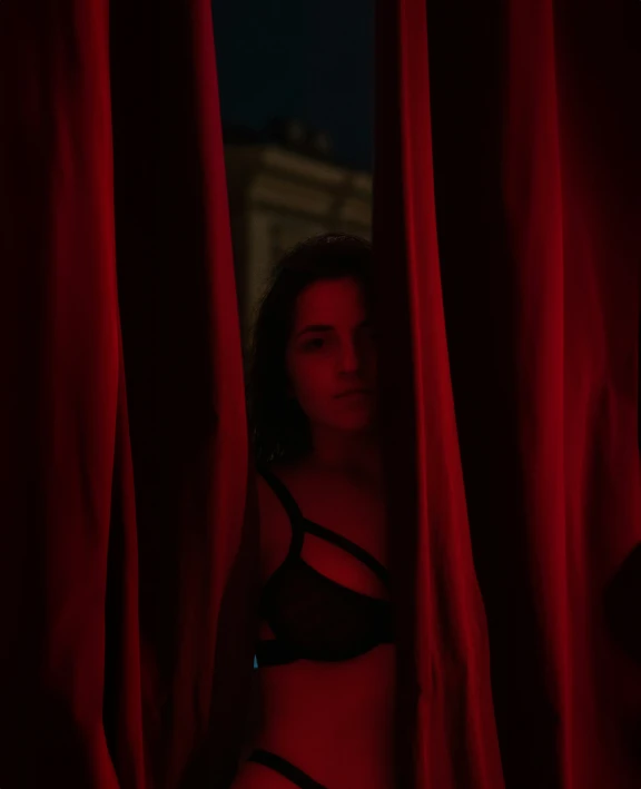 a woman in a bikini hiding behind red curtain