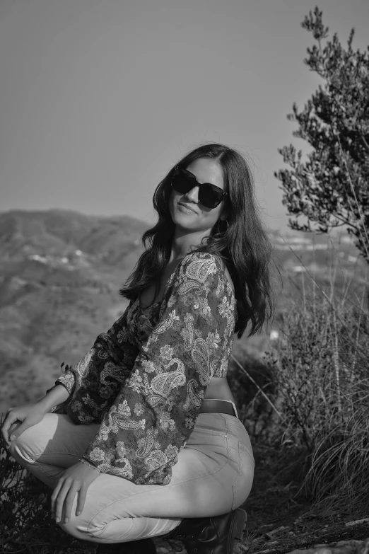 a woman sitting on a rock with sunglasses and long hair