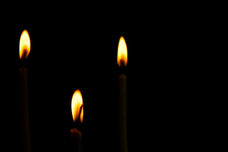 three lit candles in a row against a black background