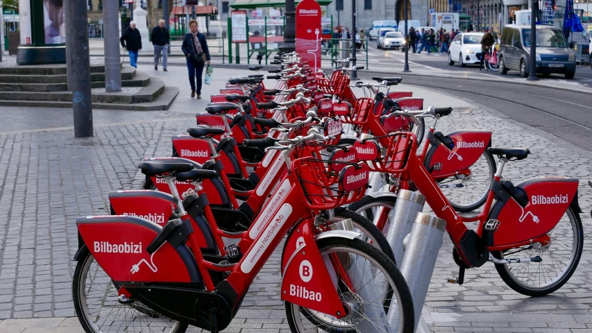 row of red bicycles are lined up in the sidewalk