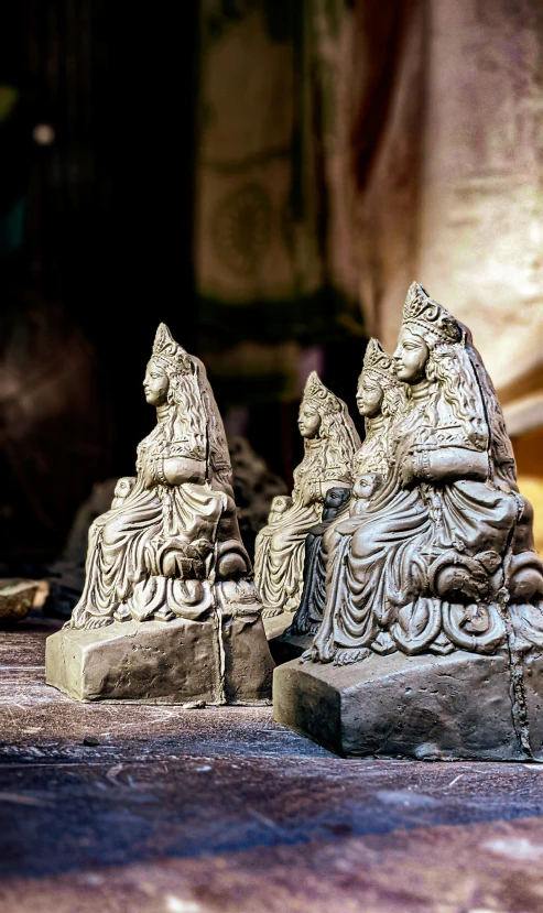 sculptures of buddha, sitting on concrete beside wall