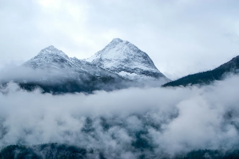 a snow covered mountain sits above clouds in the middle of a landscape