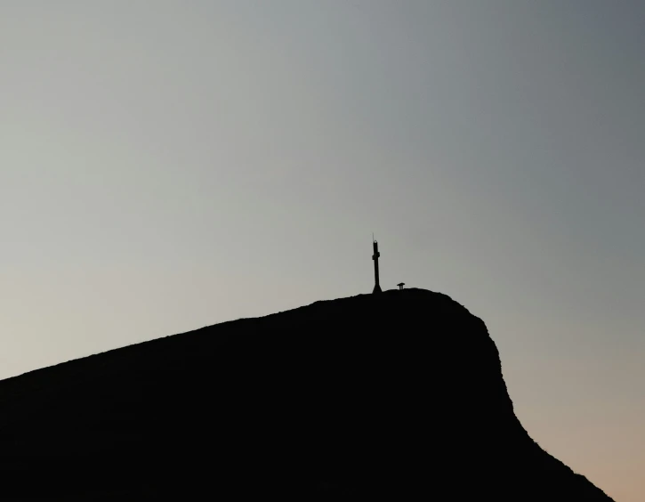 a lone black cross is on top of a hill