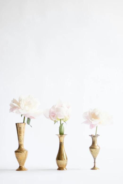 a group of three gold vases holding pink and white flowers