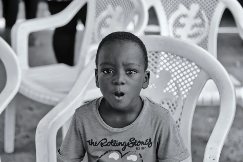 a little boy sitting on a white chair with his tongue out