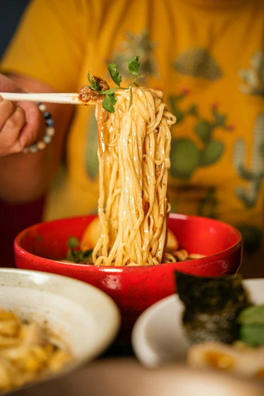 a person eating noodles with chopsticks in a bowl