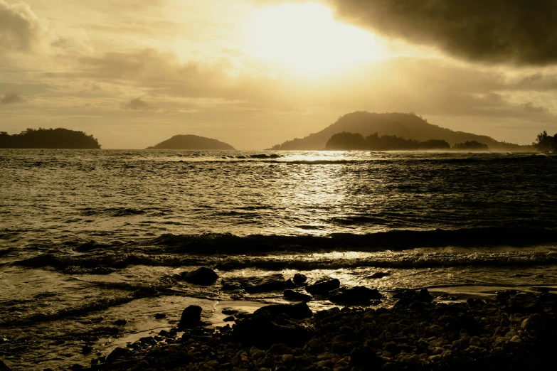 a sun set over an island on a rocky beach