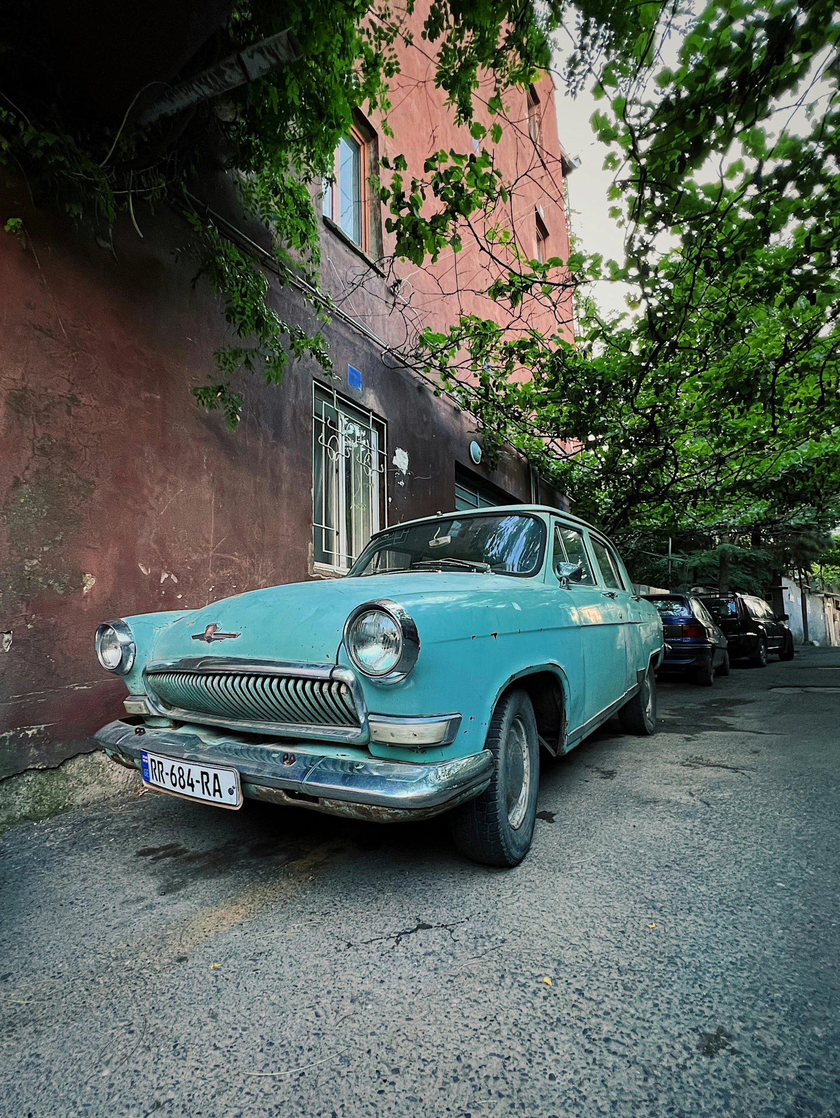 an old blue car parked next to a brown building