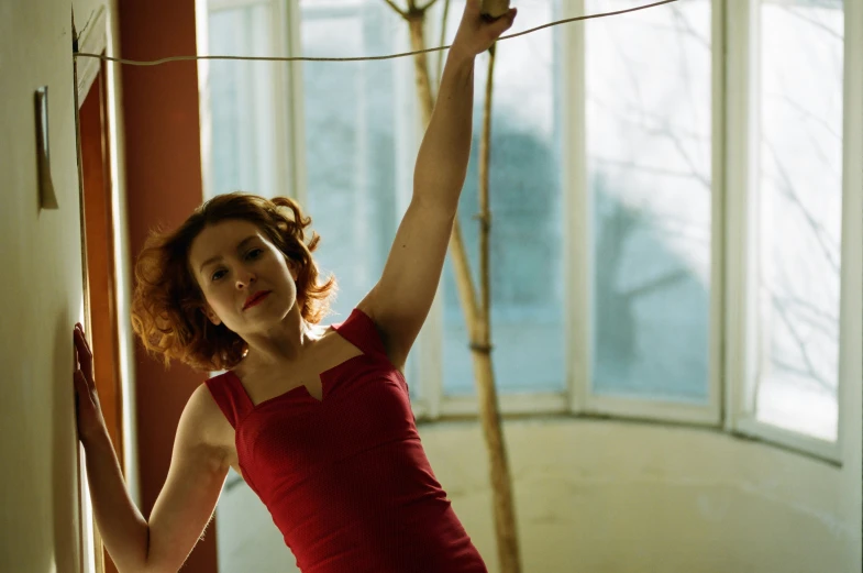 a woman in red dress posing in front of a window with her arms up