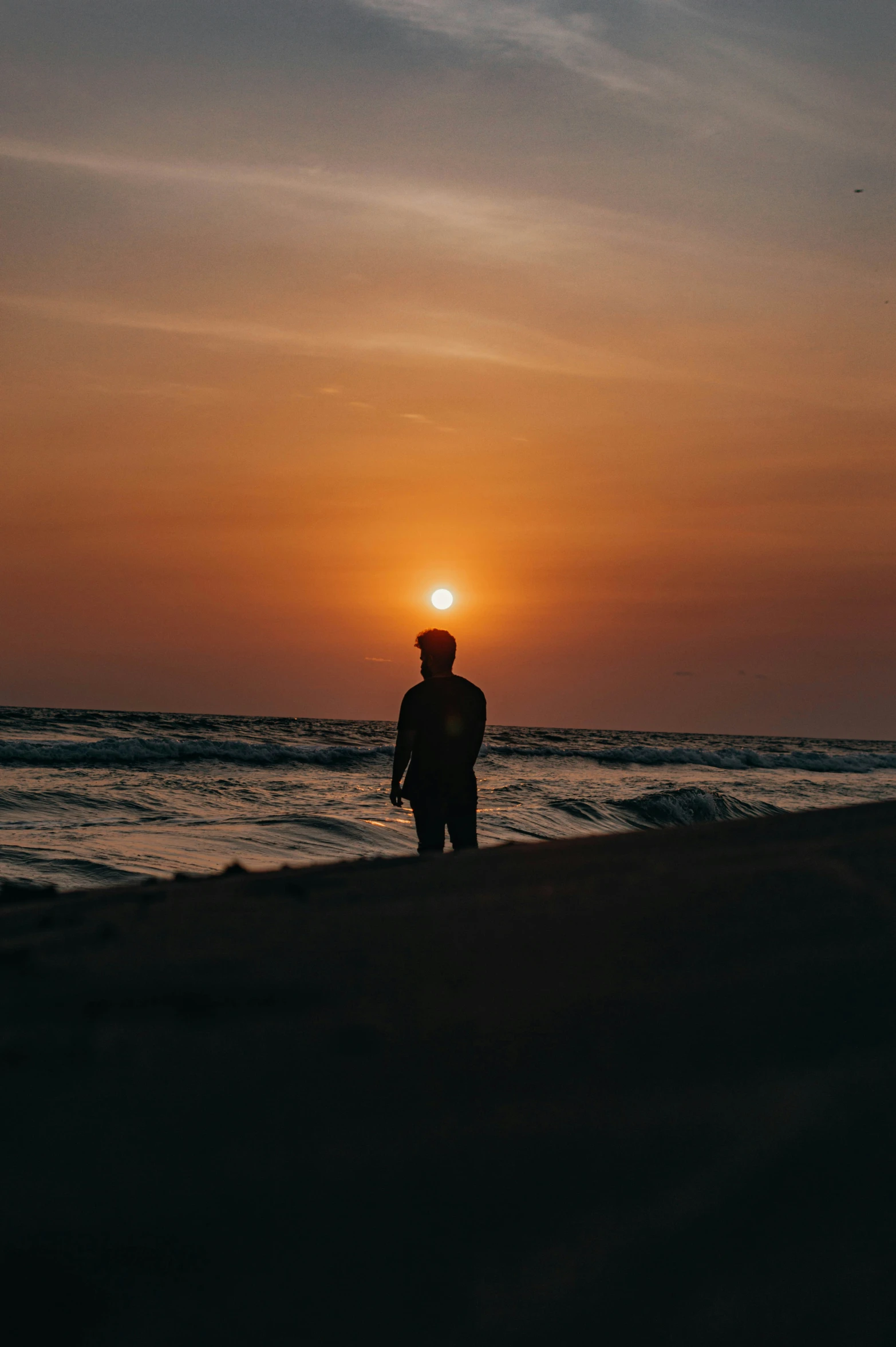 a man on the beach looking out at the sunset