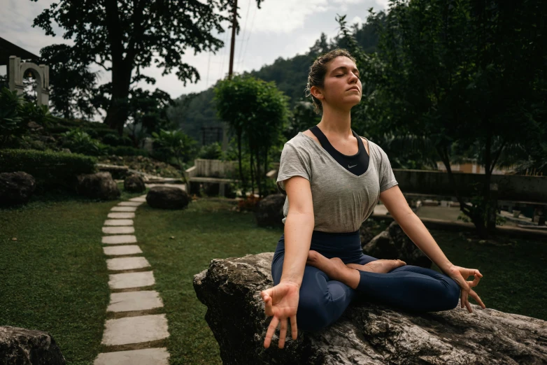 a woman is meditating on top of a rock in the middle of a grassy area