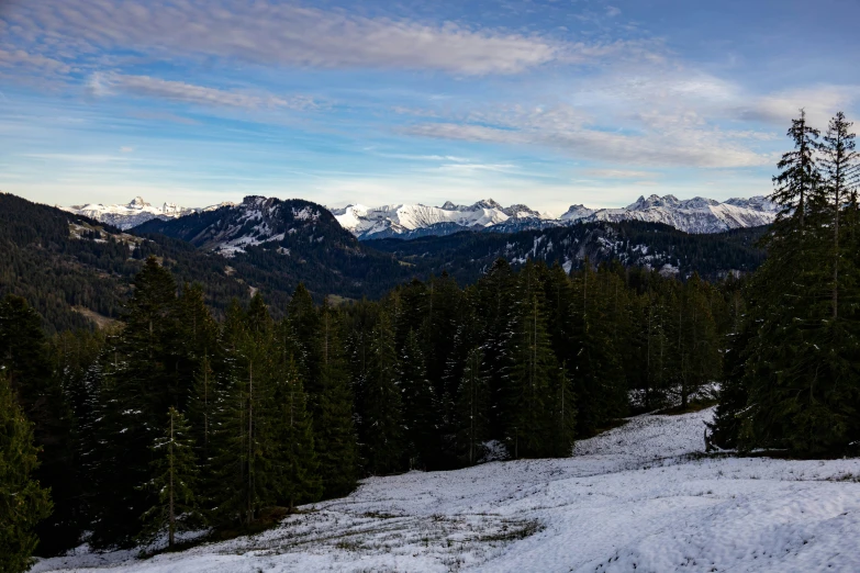 the sky is filled with clouds as snow covers mountains and evergreen trees