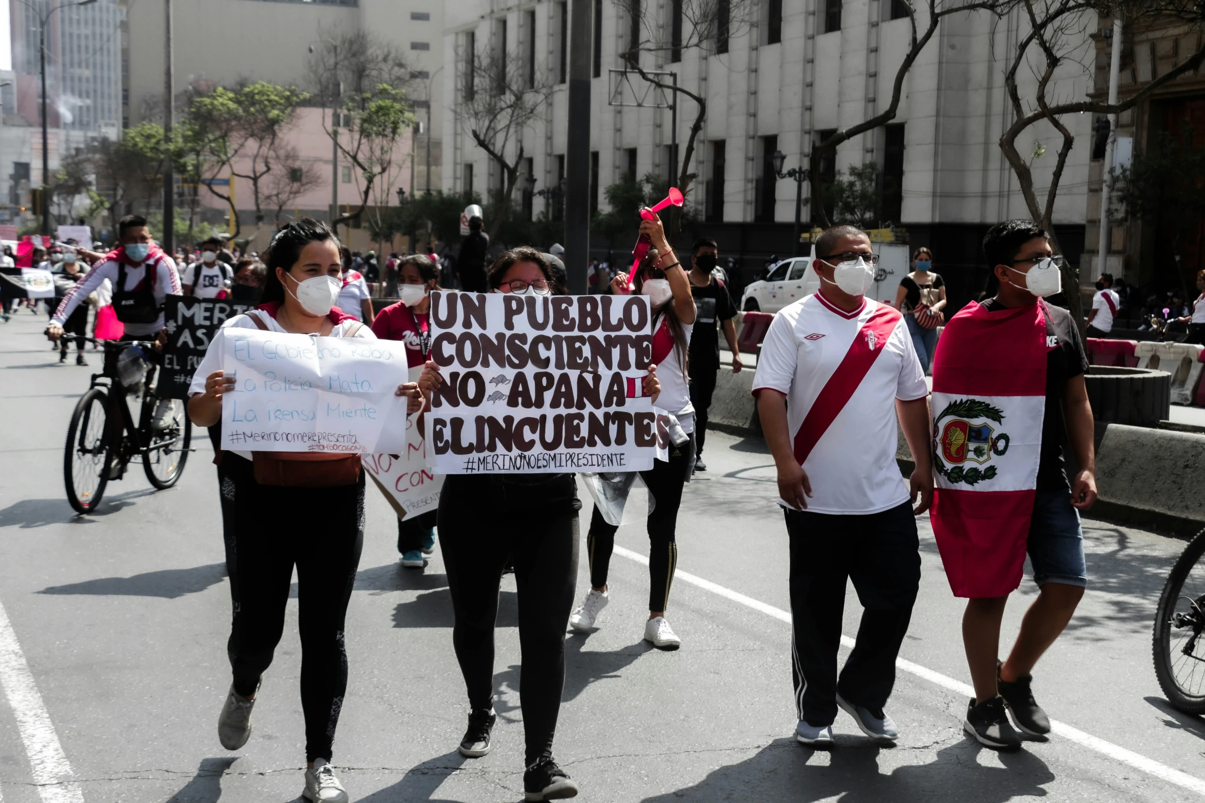 men with a protest sign and a woman holding a red - handled stick walk down a street with protest signs in spanish