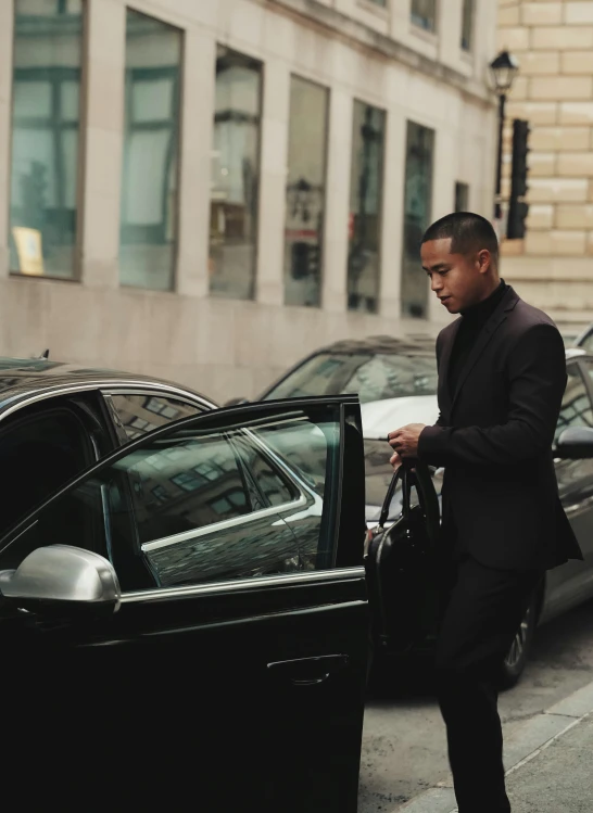 man in black outfit unloading a car on street