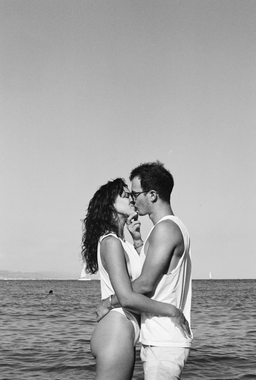 a man and woman kissing in front of the ocean