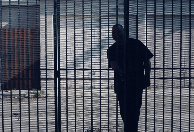 a man standing behind a tall fence next to a street